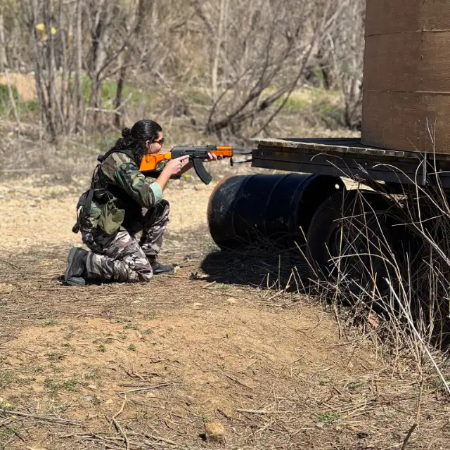A player kneels by a barrel and aims